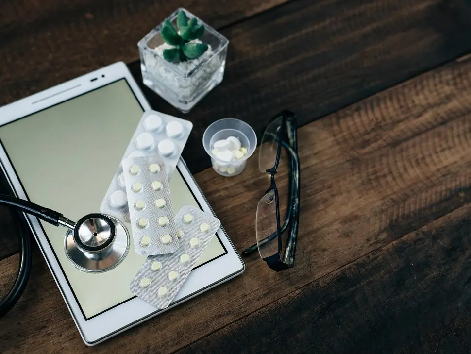 Prescription medicines, a tablet device, stethoscope and glasses on a wooden desk  -  secure RX upload